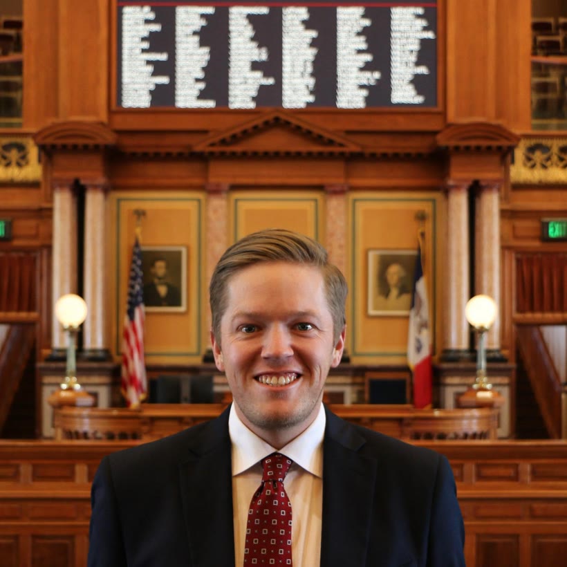 Austin Harris on the Iowa House floor, the electronic vote board lit behind him